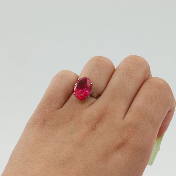 a woman's hand holding a ring with a large red stone in the middle