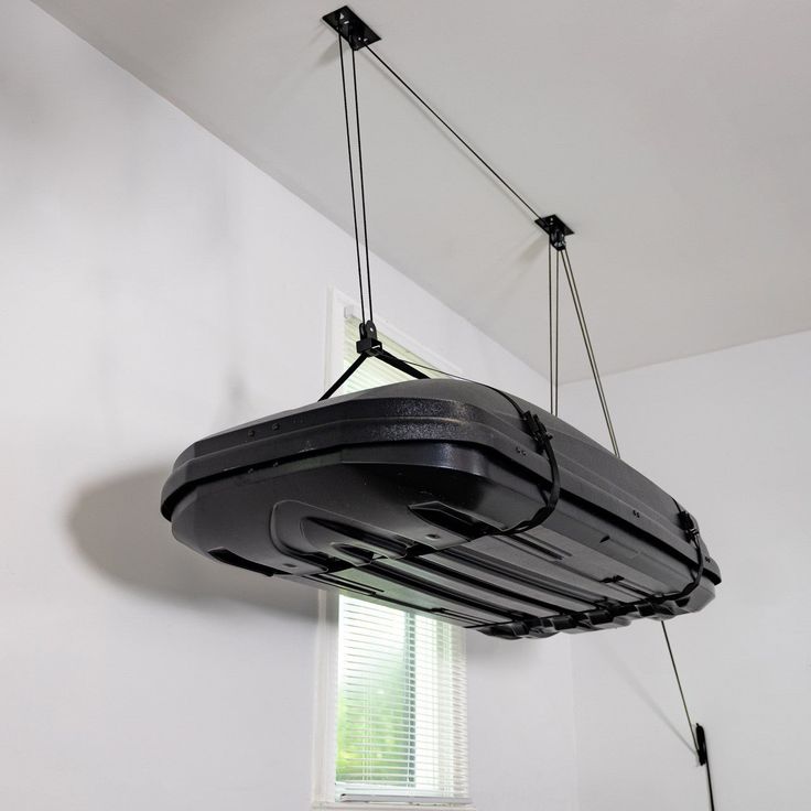 a black object suspended from the ceiling in a room with white walls and window blinds