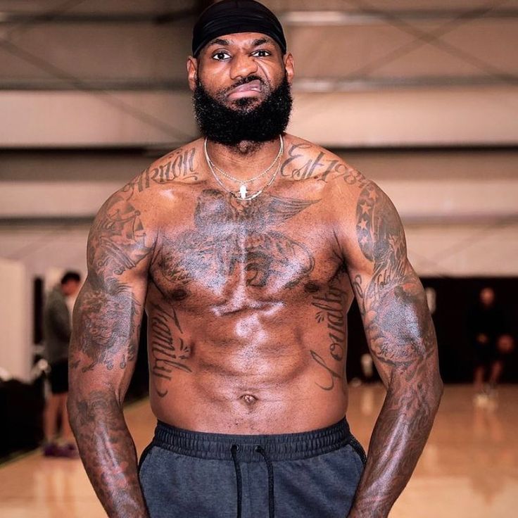 a man with tattoos on his chest standing in front of a basketball court and looking at the camera