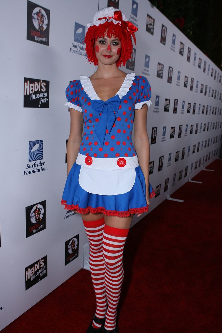 a woman with red hair wearing a blue dress and striped tights stands on a red carpet