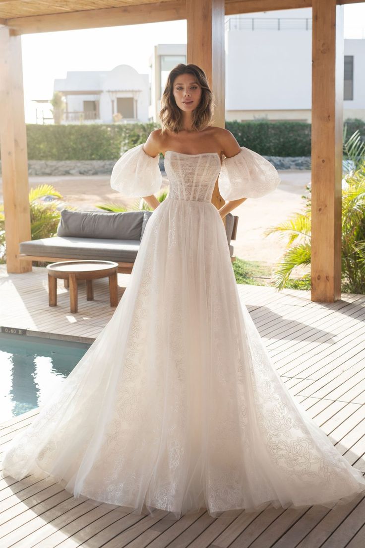 a woman in a wedding dress standing on a deck next to a pool with her arms outstretched