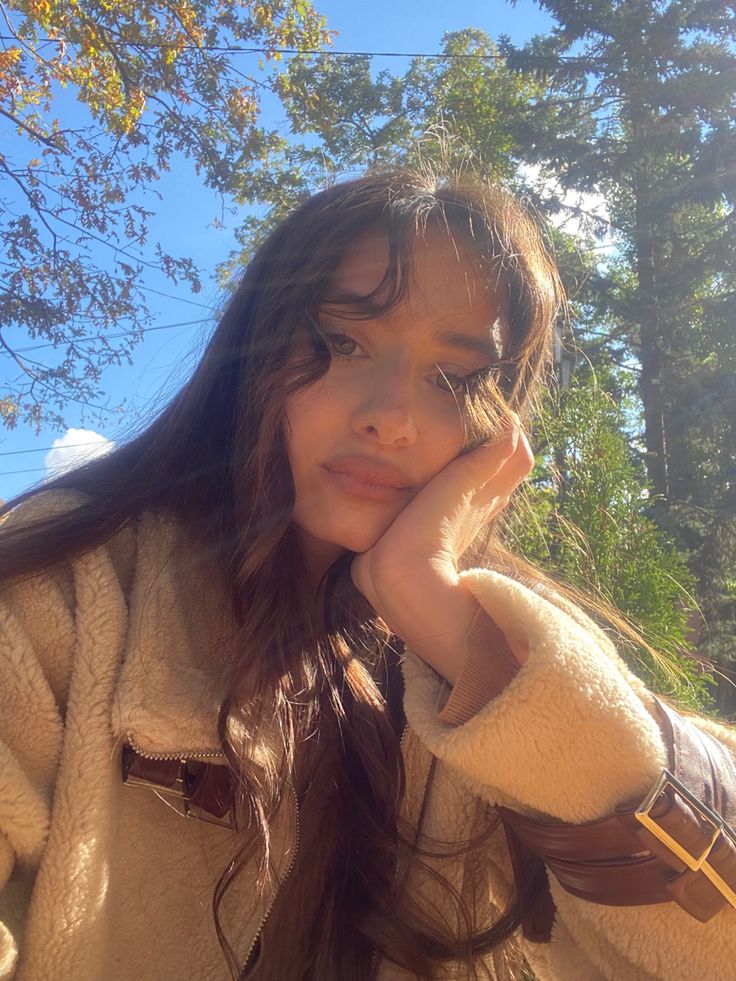 a woman with long brown hair is posing for a photo in front of some trees