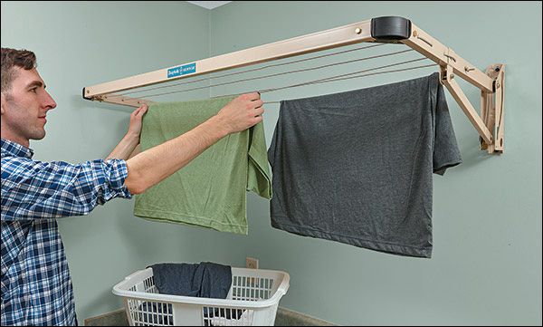 a man hanging clothes on a clothes line in his laundry room with a hamper next to him