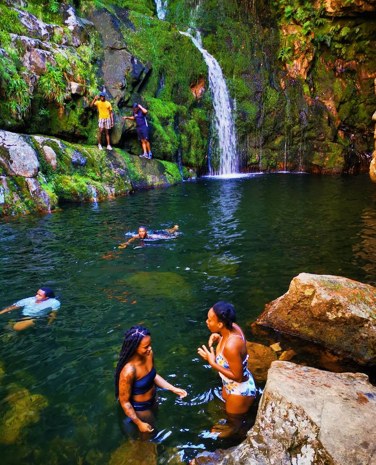 people are swimming in the water near a waterfall