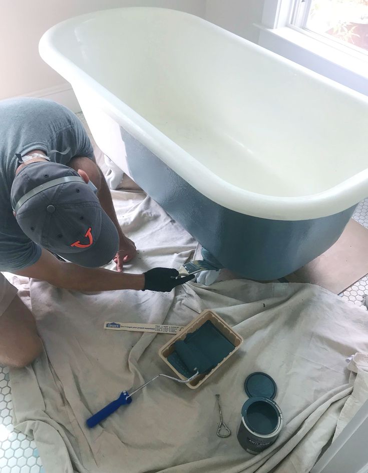 a man in grey shirt and hat painting a bathtub