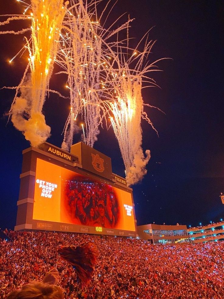 fireworks are lit up in the sky above a large crowd at a football game as people watch