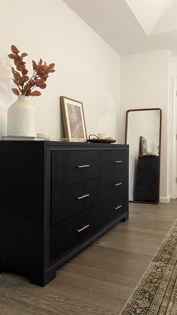 a black dresser sitting on top of a hard wood floor next to a white vase