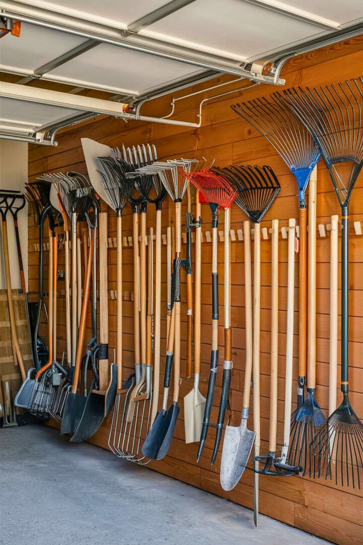 there are many shovels and rakes hanging on the wall