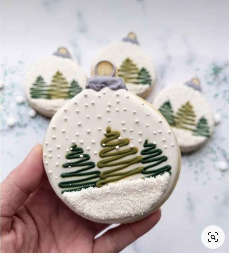 someone is holding some decorated cookies with trees on them and snow flakes all around