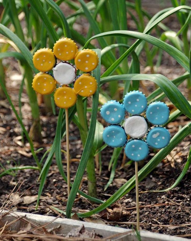 two plastic flowers sitting in the dirt next to some green grass with text overlay that says bottle cap garden art an easy earth day craft