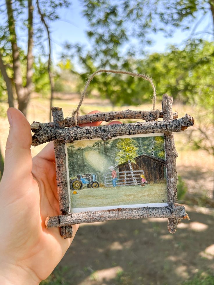 a person holding up an old photo frame in the air with trees and grass behind it