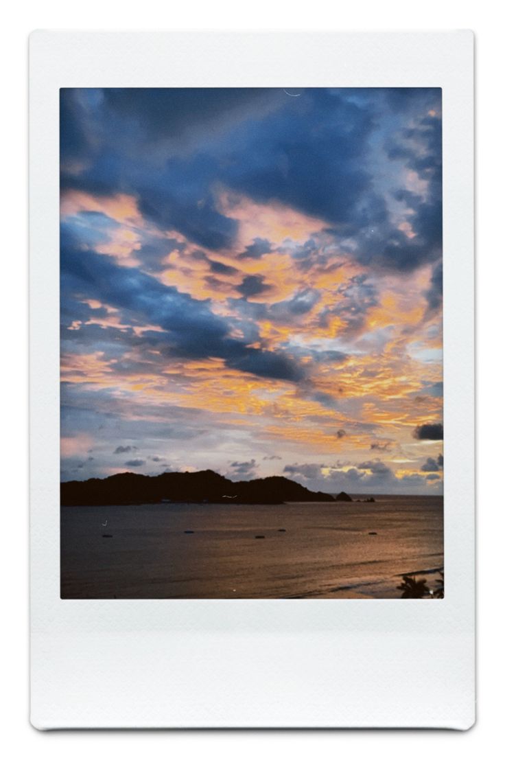 the sky is filled with colorful clouds as the sun sets over an island in the distance