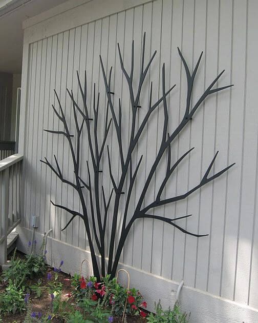 a metal tree sculpture sitting on the side of a white building next to a window