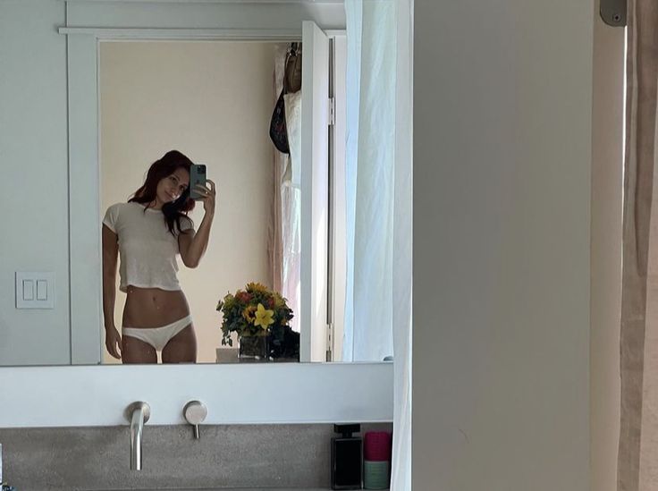 a woman taking a selfie in front of a bathroom mirror