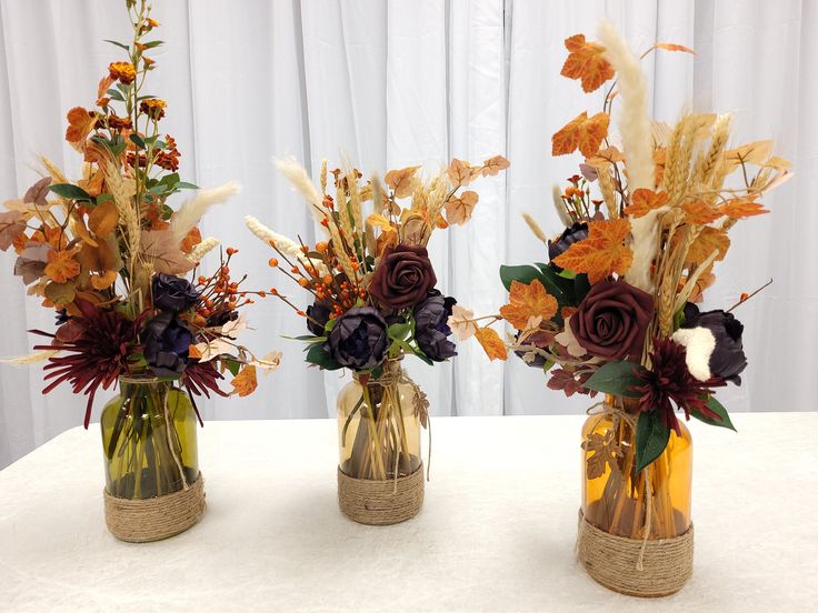 three vases filled with flowers on top of a white table covered in cloth and burlap