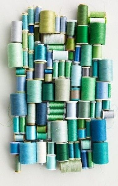 several spools of thread are arranged on a wall with green and blue colors