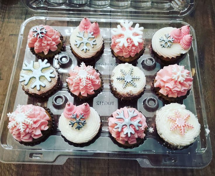 twelve cupcakes with frosting and snowflakes on them in a plastic container