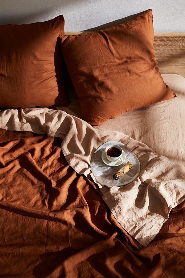 a cup of coffee sits on an unmade bed with two pillows and a blanket