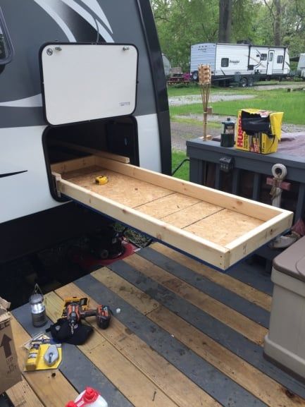 a camper with the door open and some tools on the ground