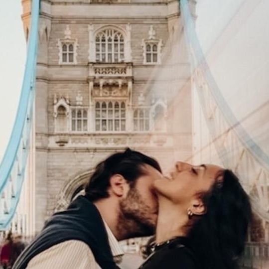 a man and woman kissing in front of the tower bridge