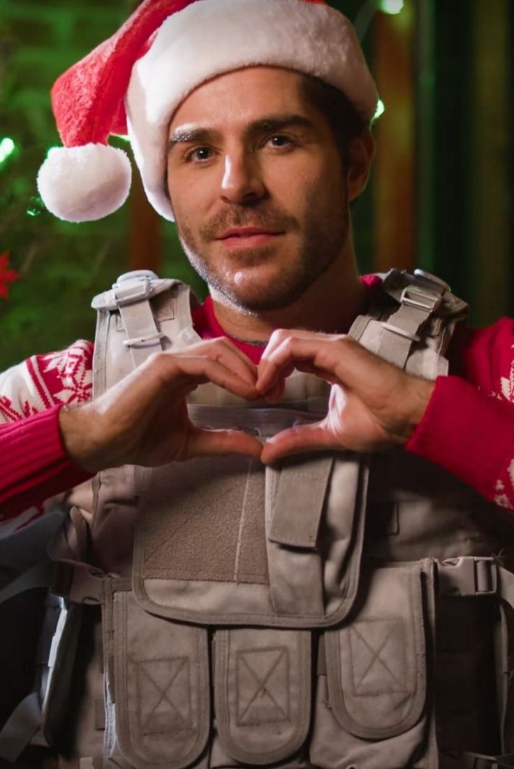 a man in a santa hat making a heart shape with his hands while sitting down