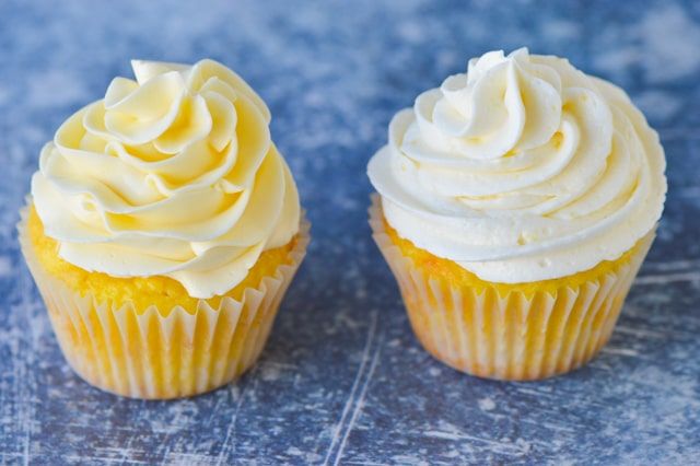 two cupcakes with white frosting sitting on a table