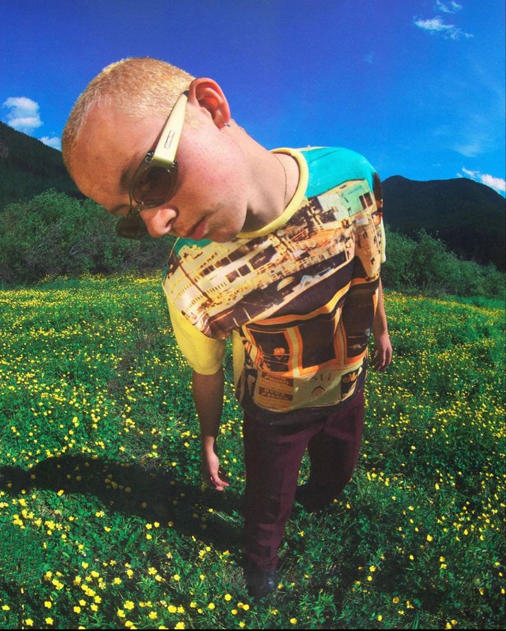 a man with sunglasses on his head standing in the middle of a field full of yellow flowers