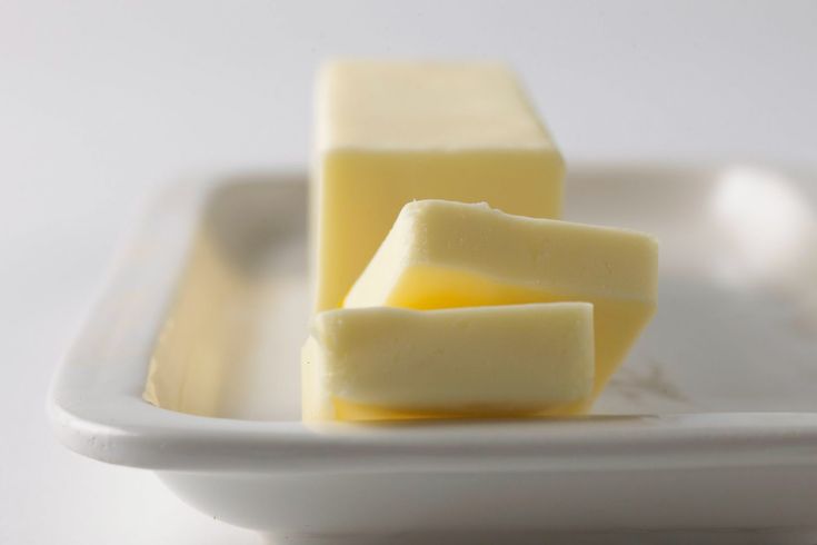 three cubes of butter on a white plate, with one piece cut in half