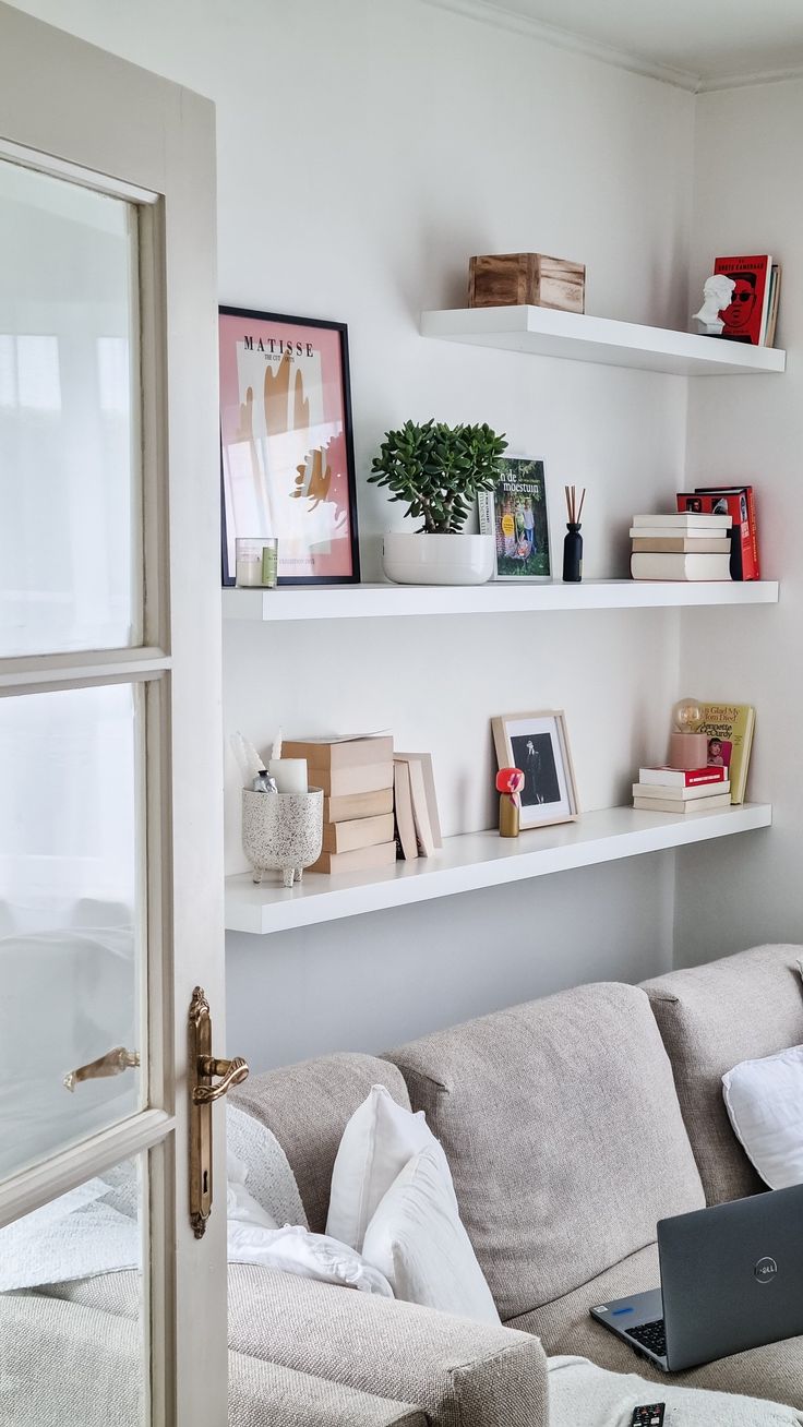 a laptop computer sitting on top of a white shelf in a living room next to a couch