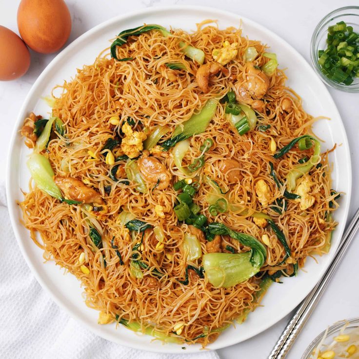 a white plate topped with noodles and veggies next to an egg on a table