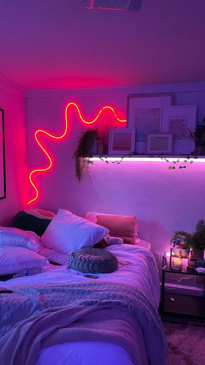 a bed with pillows and blankets in a room lit up by neon lights on the wall