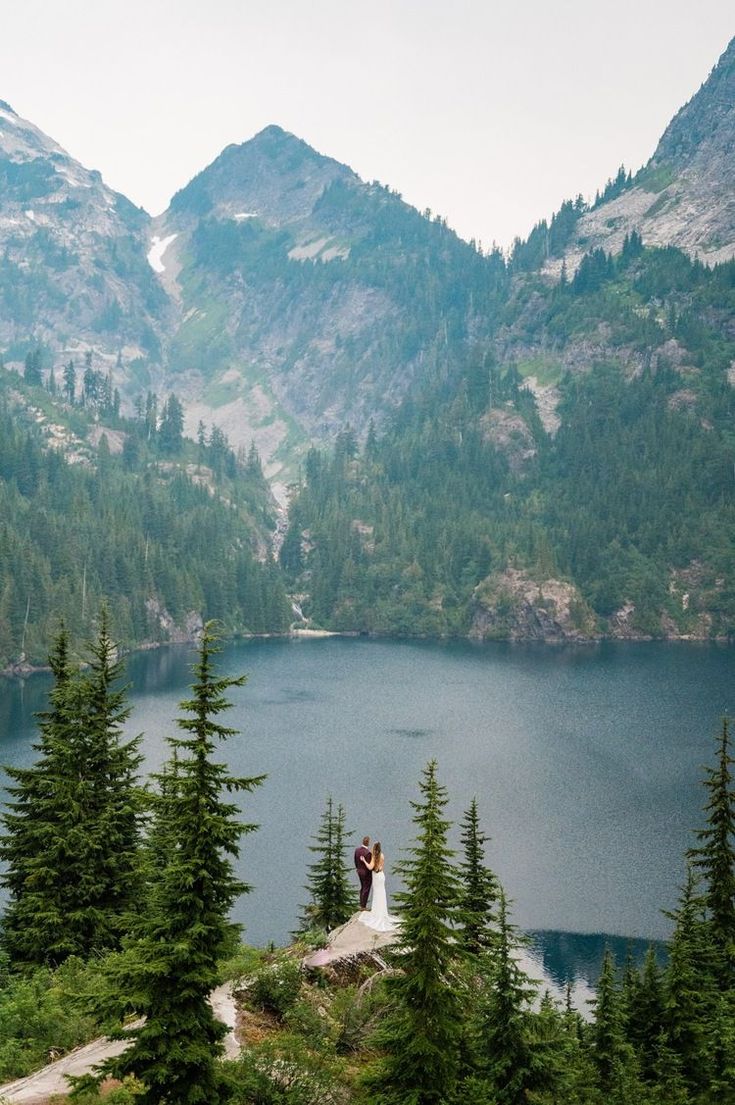 two people standing on top of a mountain overlooking a lake