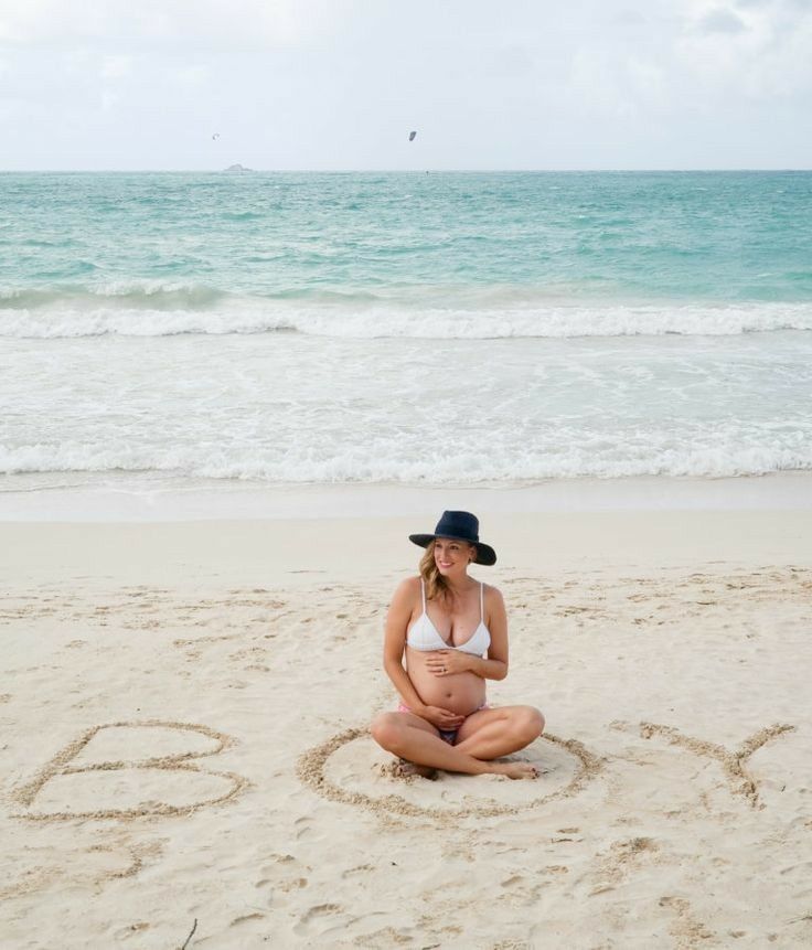 a woman sitting in the sand at the beach with her name written in the sand