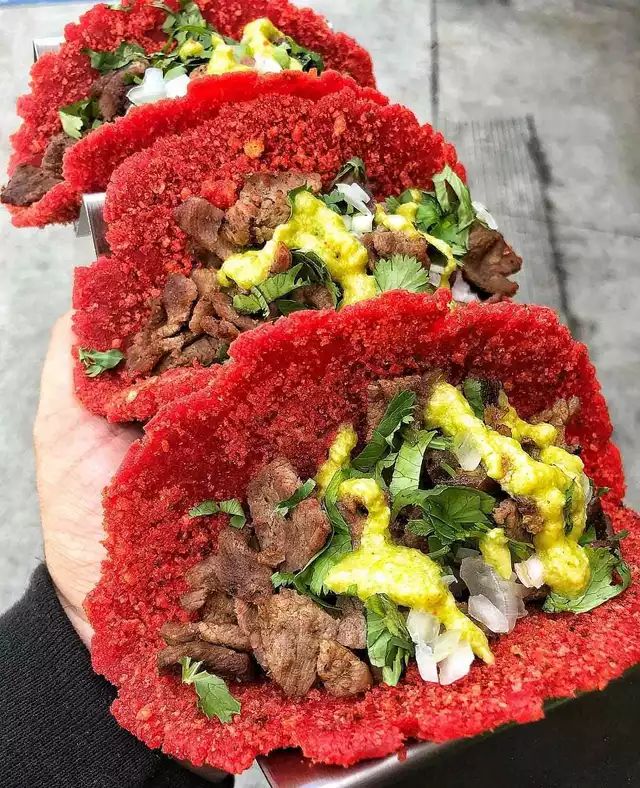 a person holding three red breads with meat and vegetables on them