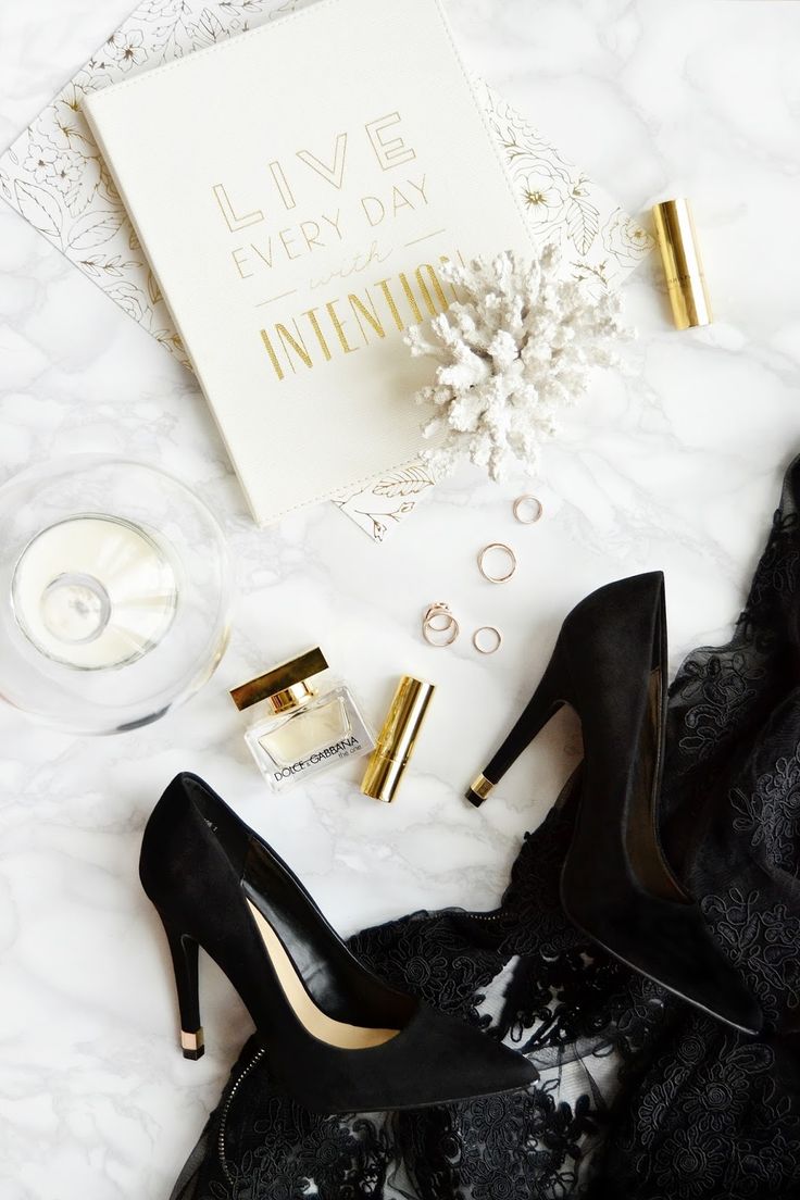 black high heel shoes on top of a white table next to an open notebook and perfume bottle