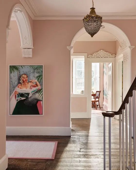 a hallway with pink walls and wooden flooring next to a chandelier hanging from the ceiling