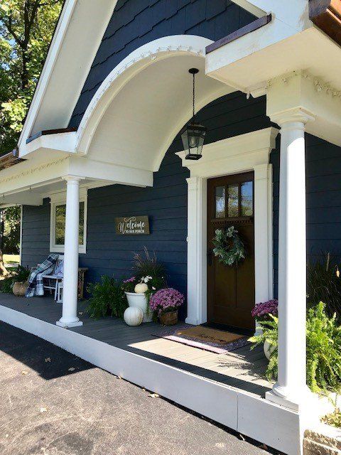 a blue house with white pillars and flowers on the front porch, along with potted plants