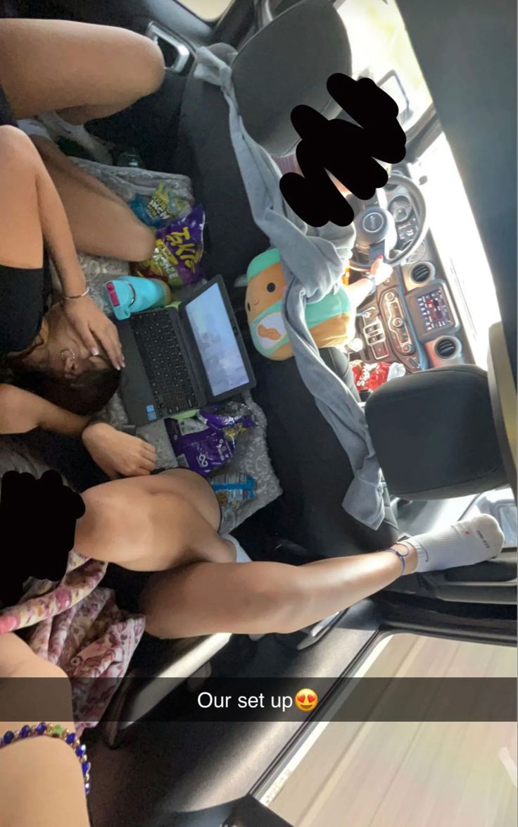 two women sitting in the back seat of a car with their feet up and one holding a cell phone