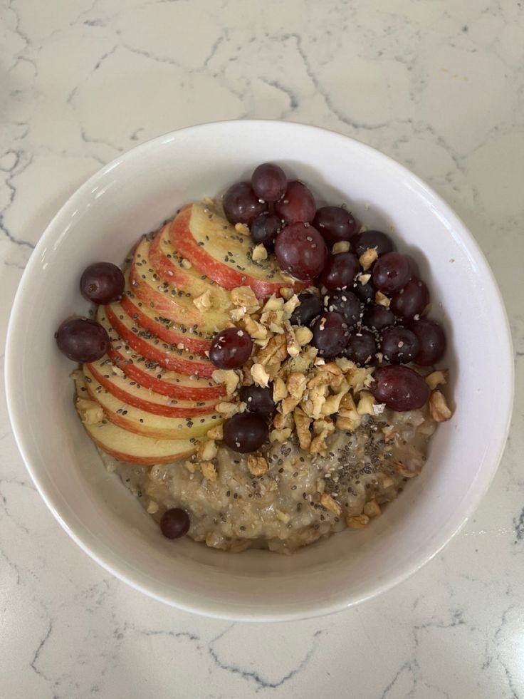 a bowl filled with oatmeal topped with apples and grapes