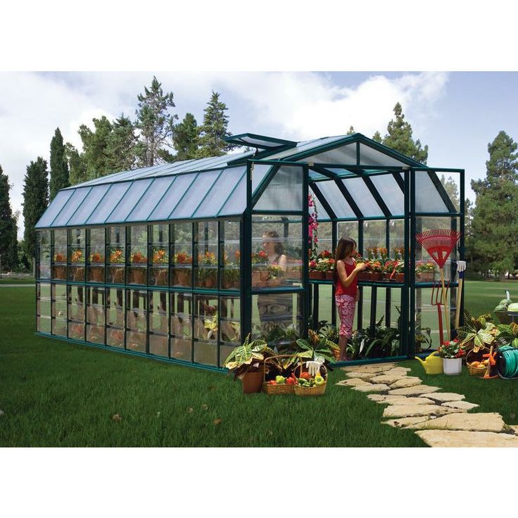 a woman standing in front of a green house filled with flowers