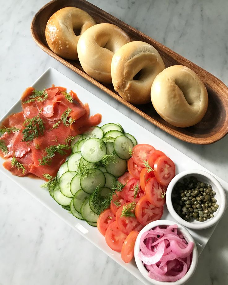 an assortment of vegetables and bagels sit on a white plate next to a wooden tray