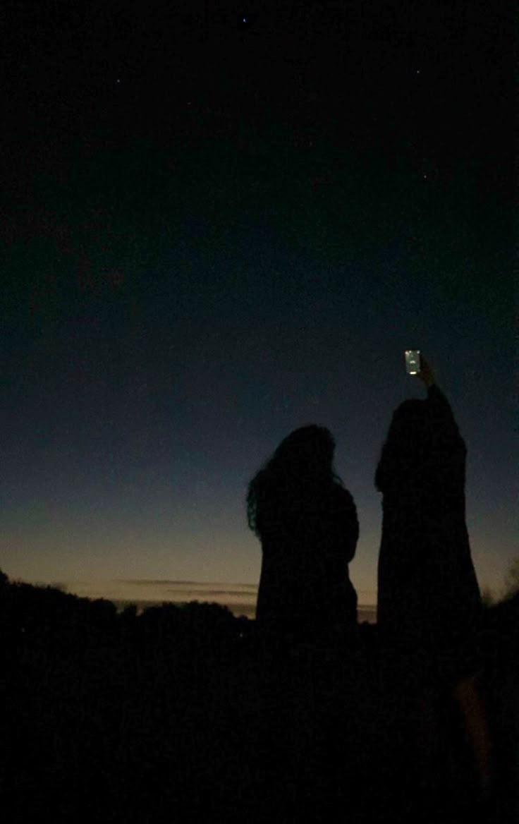 two people standing next to each other at night with their cell phones in the air