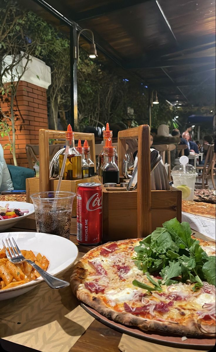 two pizzas sitting on top of a table next to plates of food and drinks