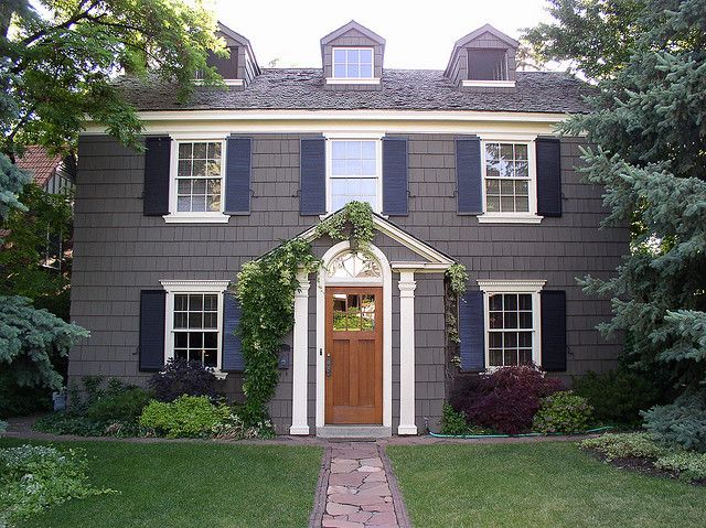 a large gray house with white trim and black shutters on the front door is surrounded by greenery