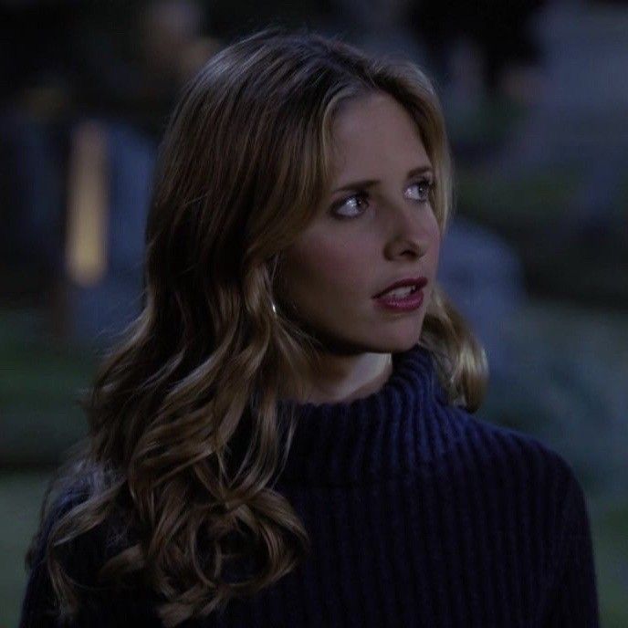 a woman with long hair wearing a blue sweater and looking off to the side while standing outside at night