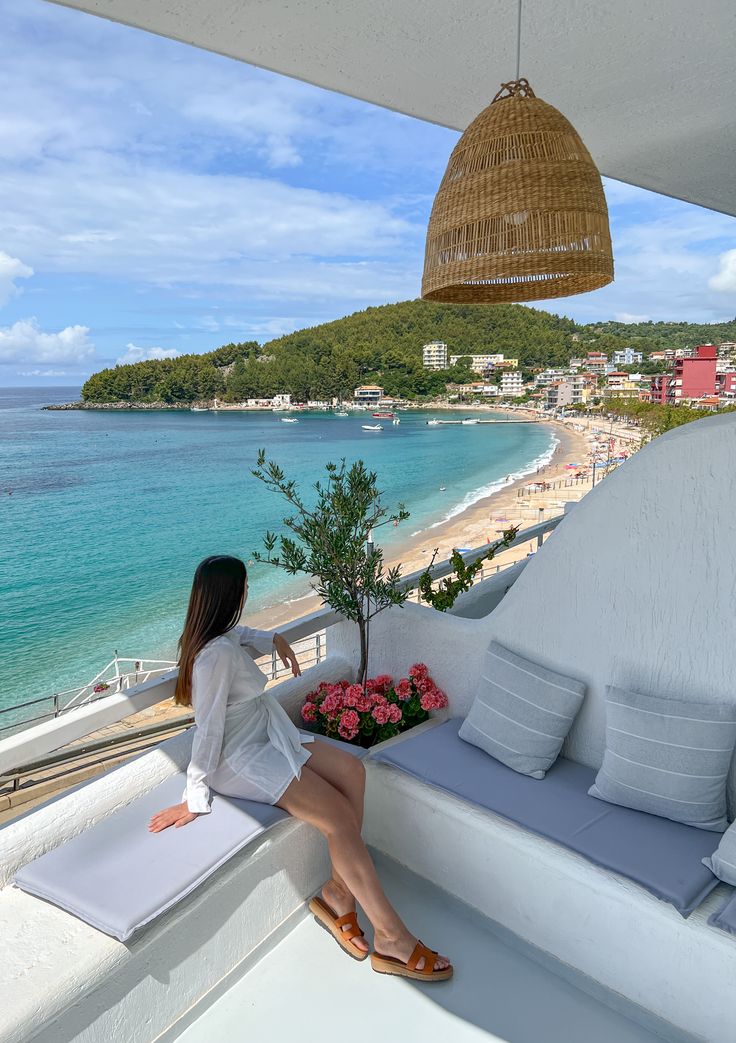 a woman sitting on top of a balcony next to the ocean with flowers in front of her