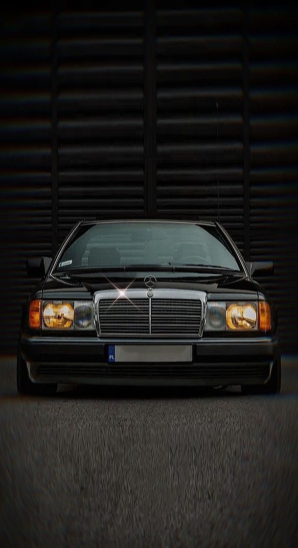 a black car parked in front of a garage door with it's lights on