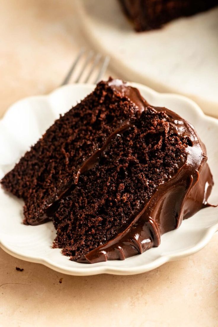 a slice of chocolate cake on a white plate with a fork in front of it