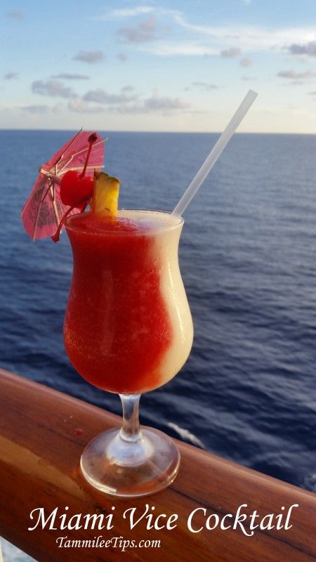 a red drink sitting on top of a wooden table next to the ocean