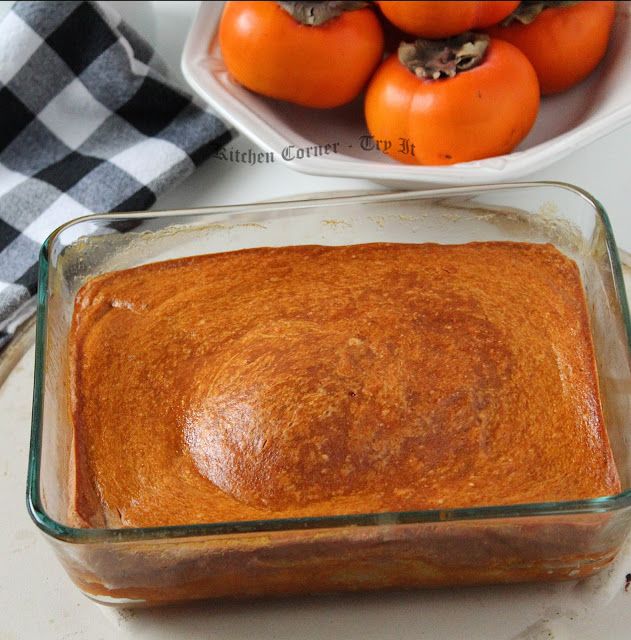 a casserole dish with tomatoes in the background and a bowl full of oranges behind it